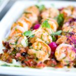 Closeup of delicious shrimps with vegetables and microgreens on white plate on catering table